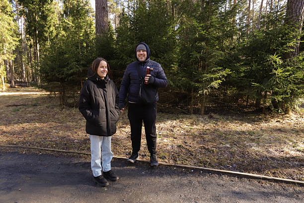 istock Two people dressed for the cold weather stand side by side in a forest park, with one holding a thermos and the other appearing relaxed and calmâan ideal metaphor for friendship, travel, and outdoor therapy. 2217599009