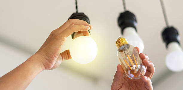 istock Power saving concept. Hands holding new Light Emitting Diode ( LED ) light bulb with light on and blur spiral compact-fluorescent (CFL) bulbs behind for copyspace. 2217602307