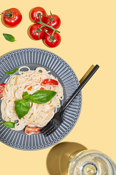 istock Creamy spaghetti with tomatoes, cheese and basil on a plate on a yellow background 2217606153