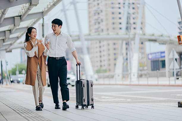 istock Two Asian professionals stand outside a station, sharing a phone screen while conversing, possibly waiting for a ride or meeting a colleague. This scene highlights the flexibility of modern business, where digital technology enables seamless collaboration 2217612785