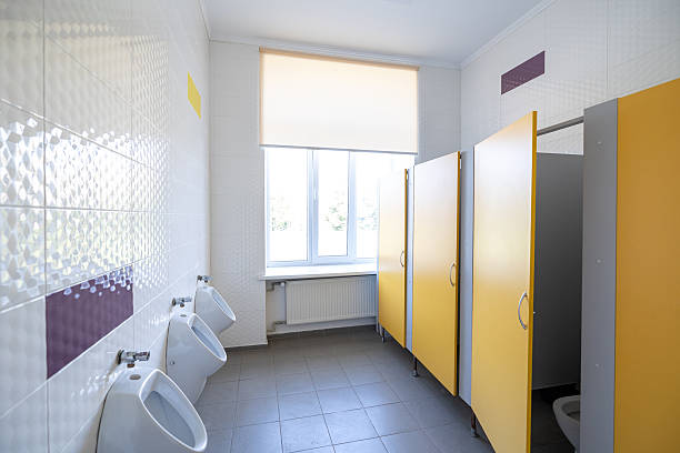 istock A modern schoolboys' restroom with white tiled walls and yellow partitions, including several urinals and a window. Toilet stalls are present. The space is clean 2217613302