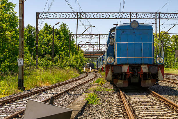 istock vintage blue diesel locomotive stands on railway tracks surrounded by greenery, under a network of overhead power lines. The train is stationary, captured in bright daylight 2217618102