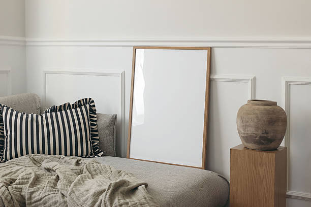 istock Blank thin wooden picture frame leaning against white stucco molding wall. Minimal elegant poster mockup. Artistic template. Grey sofa, ruffled pillow. Wooden pedestal, clay vase. Scandinavian interior 2217620165