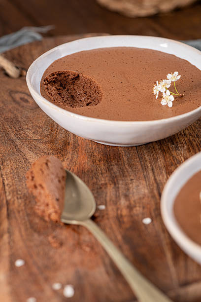 istock Individual servings of smooth chocolate mousse in white bowls, one with a spoonful being lifted, garnished with tiny white flowers, set on a rustic wooden board 2217620846