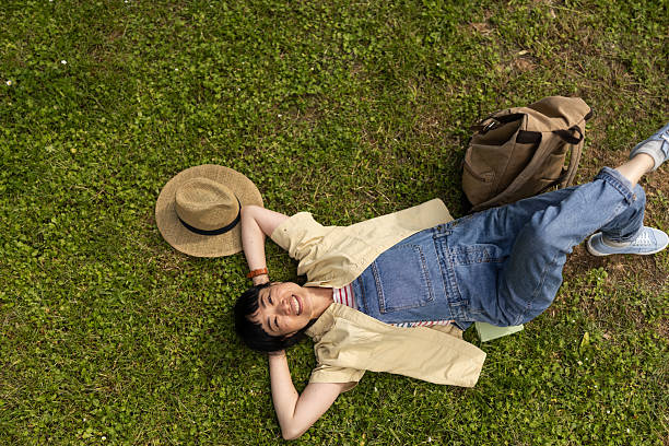 High angle shot of smiling Asian woman lying on grass and looking at camera while relaxing in nature