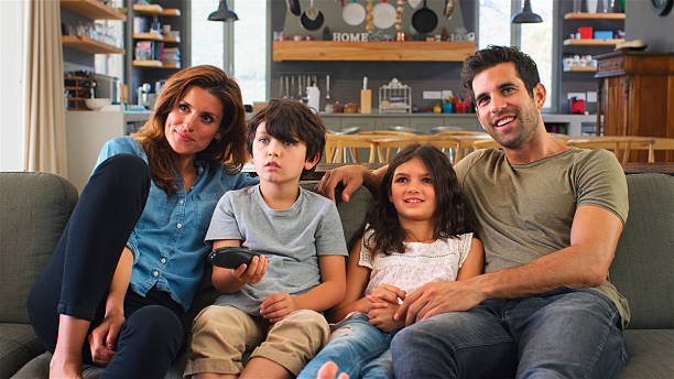 istock Family Sitting On Sofa In Open Plan Lounge Watching Television 2217626939