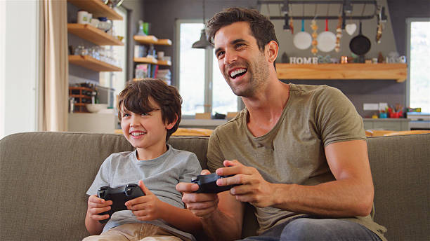 istock Father And Son Sitting On Sofa In Lounge At Home Playing Video Game 2217626966