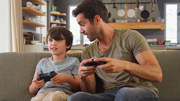 istock Father And Son Sitting On Sofa In Lounge At Home Playing Video Game 2217627003