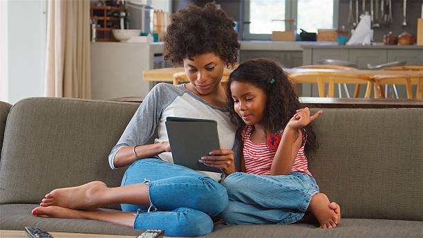 istock Mother And Daughter Sit On Sofa In Lounge Using Digital Tablet 2217627019