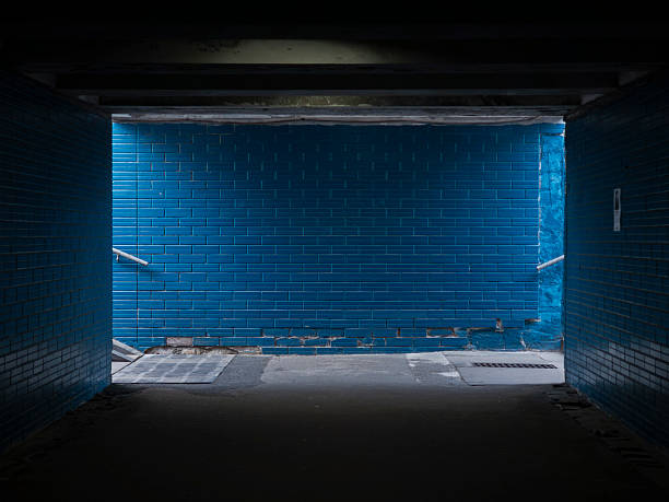 Empty dark subway with blue tiled wall and illuminated area at the end creating mysterious atmosphere