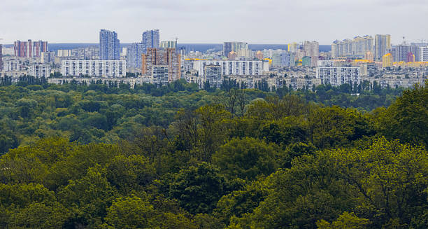 istock Green forest extending in front of Kyiv cityscape under cloudy sky 2217631232