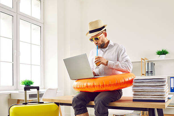 Business man sitting in office with beach ring and suitcase and booking holiday tickets online stock photo
