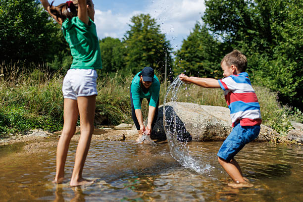 Three individuals having fun splashing water at a shallow stream on a sunny day, showing joy, connection, and excitement.