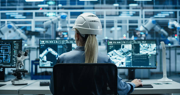 istock Female Industrial Engineer Working Behind a Desk in a Modern Manufacturing Facility with Automated Robotic Arms. Specialist Monitoring Circuit Board Assembly Line and Optimizing Production Output 2217640671