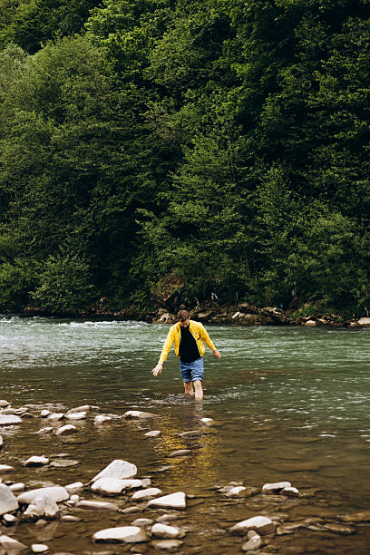 istock Young man in a yellow jacket standing knee-deep in a mountain river. 2217641181