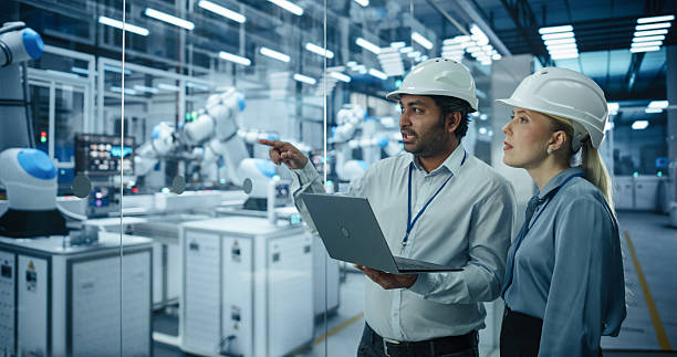 istock Two Engineers, a South Asian Male and a Caucasian Female, Collaborate Using a Laptop Computer to Optimize Robotic Systems in a Modern Factory, Analyzing Productivity and Automation 2217641461