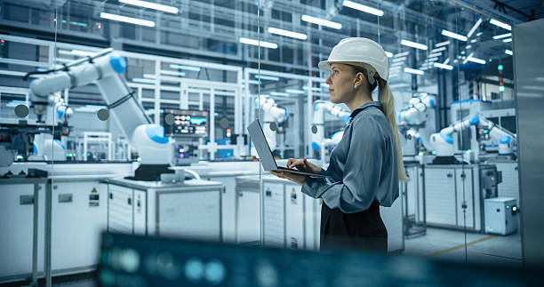 istock Industrial Systems Administrator Working on Laptop Computer at a Modern Manufacturing Plant. Female Developer Programming the Work of the Robotic Arms, Monitoring Production on the Assembly Conveyor 2217641598