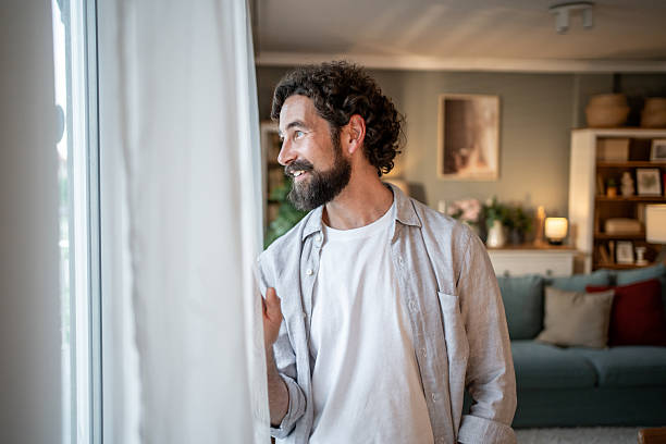 istock Happy bearded man looking out the window at home 2217650247
