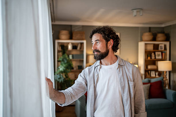 istock Thoughtful man opening curtains and looking out window at home 2217650257