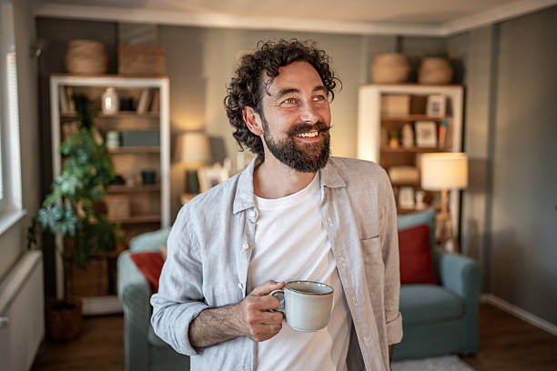 istock Smiling man drinking coffee in living room looking away 2217650329