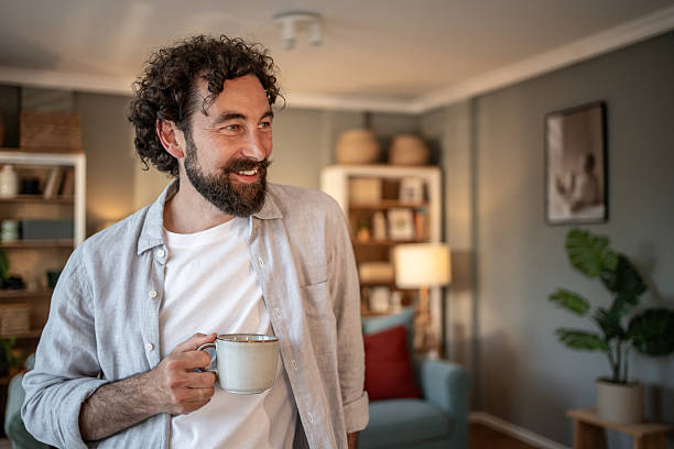 istock Smiling man drinking coffee and looking away in living room 2217650330