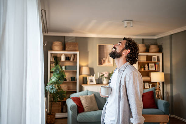 istock Happy man drinking coffee and looking upwards in living room 2217650362
