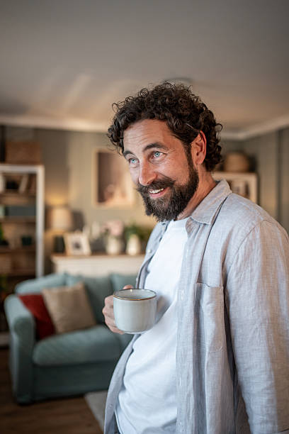 istock Smiling bearded man drinking coffee in living room 2217650370