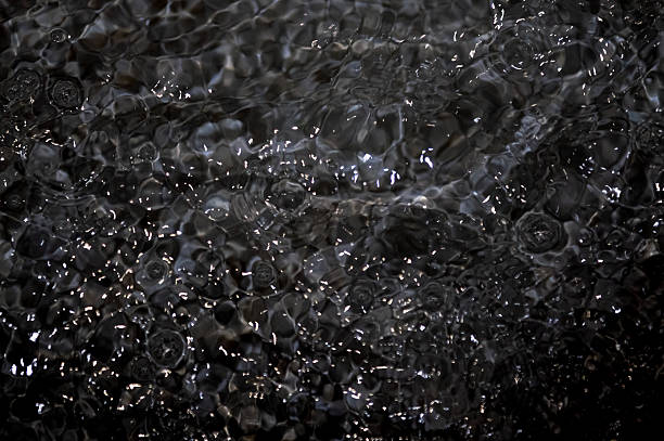 Black water with ripples. Defocus blurred black clear calm water surface texture with splashes and bubbles. Water surface background