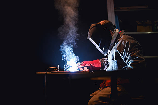 Welder working on metal piece in dark workshop creating sparks and smoke