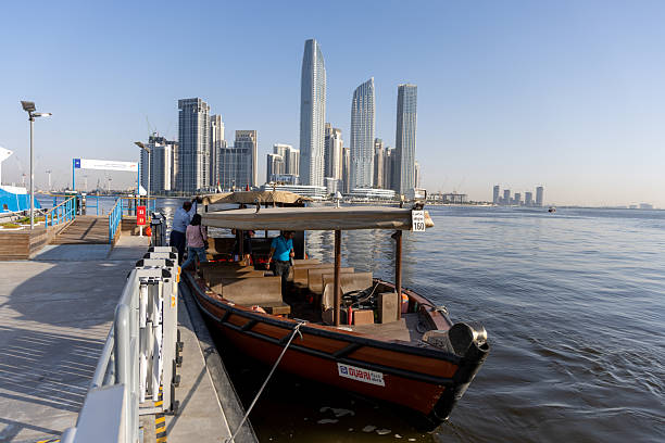 Dubai, United Arab Emirates - April 4, 2025 : People board Abra moored on the Al Jaddaf Marine Transport Station with the Dubai Creek Harbour skyline behind in Dubai, United Arab Emirates.