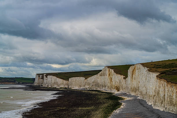 A sweeping view of the iconic Seven Sisters chalk cliffs along the English coastline, stretching dramatically against the cloudy sky and sea. This breath-taking natural landscape captures the rugged beauty of the South Downs, perfect for travel, nature, and outdoor adventure content