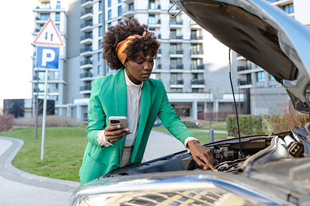 istock Woman examining car engine while holding smartphone in the city 2217665069