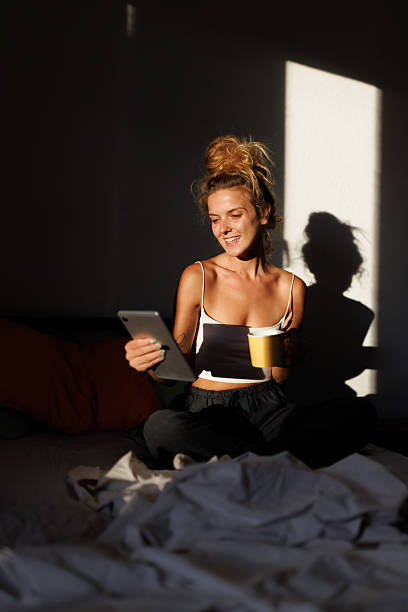 istock Woman enjoying her morning routine while sitting on the bed, using a tablet and sipping coffee in a sunlit room 2217667091