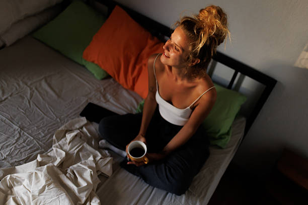 istock Bright morning with a woman enjoying a warm drink while sitting on a bed surrounded by colorful pillows in a cozy room 2217667092