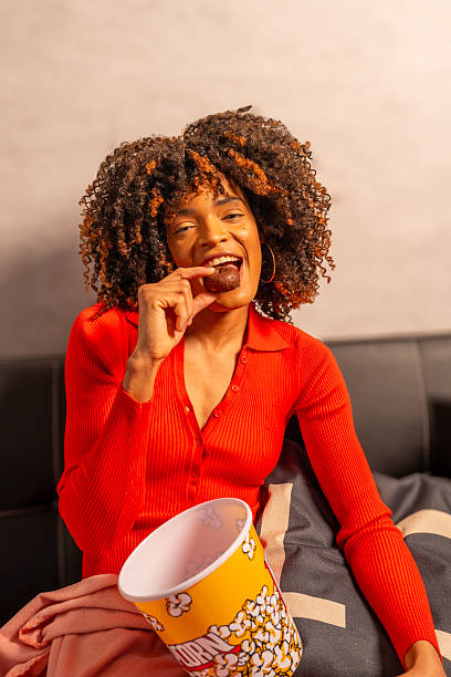 istock Young woman enjoying chocolate and popcorn on sofa 2217668099