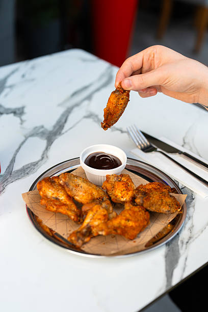 The man dips a chicken wing into barbecue sauce.
