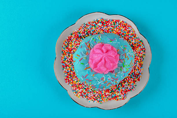 On the plate is a pink cake with multi-colored sprinkles. The plate is on a blue background.