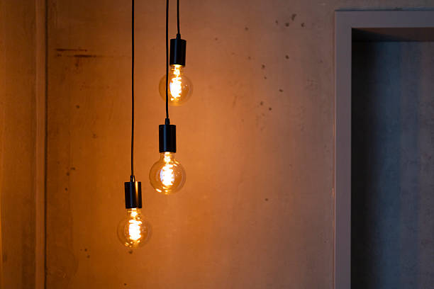 istock Three decorative hanging light bulbs are suspended from the ceiling, casting a warm glow against a textured wall. The lights enhance the cozy and modern atmosphere of the room 2217676613