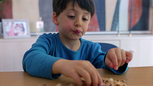 istock Young boy eating pistachio nuts at a table, carefully selecting and enjoying his snack. a simple moment of a child savoring a healthy treat, focused on the act of eating-SD 480p 2217677521