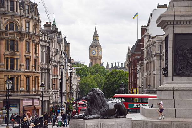 London, UK - Jul 25, 2017: A tourist riding one of the Lions statue in Trafalgar Square late in the day as people take photos.