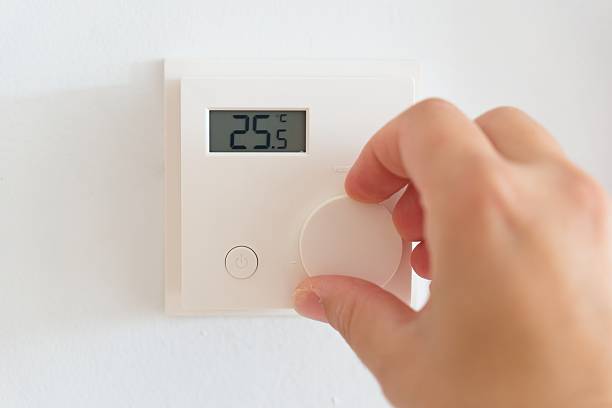 istock Hand adjusting smart thermostat on white wall, setting precise temperature for energy-efficient home climate control 2217680649