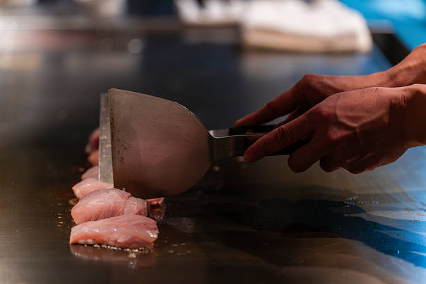 Row of shrimp and white fish fillets cooks on a teppanyaki grill.
