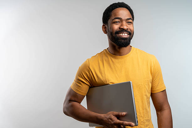 istock Young Black man smiling while holding closed laptop in hands. 2217682327
