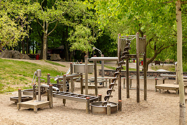 A children's playground features unique nature-inspired equipment including slides and climbing structures. Lush trees and a sandy area create a serene outdoor environment for play