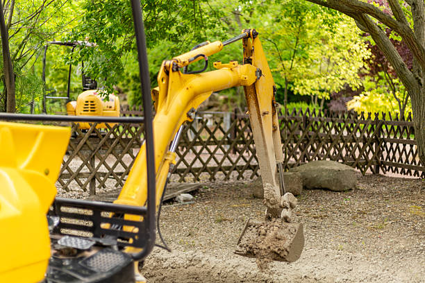 istock A yellow excavator is digging into the soil at a construction site surrounded by green trees and a wooden fence, highlighting a busy outdoor work environment 2217683657