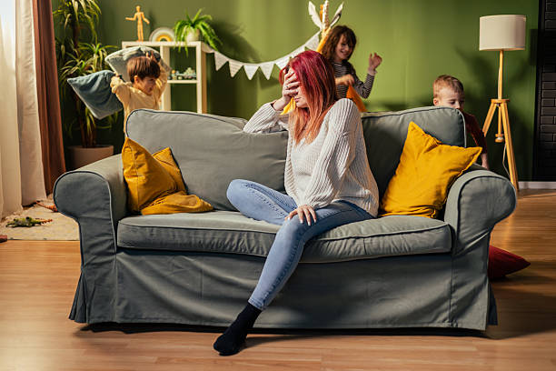 istock Stressed mother covering face while children playing at home 2217685056