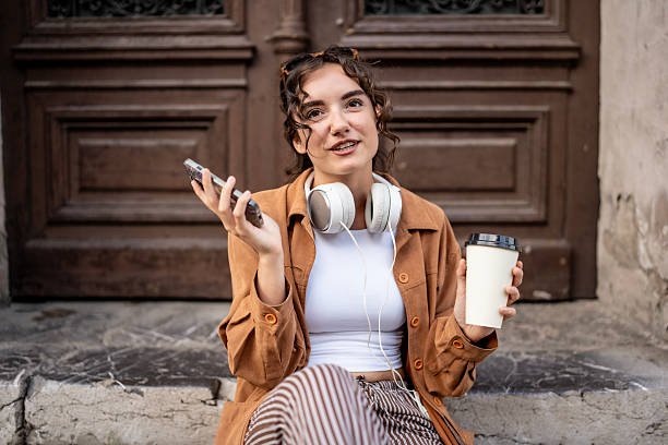 istock Young Woman Enjoying Coffee Outdoors While Using Smartphone with Headphones 2217693091
