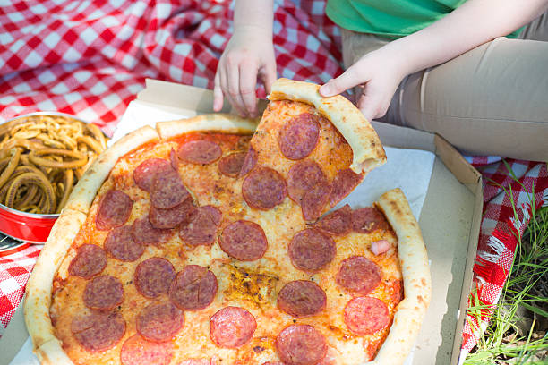 Woman eating pepperoni pizza during picnic on grass