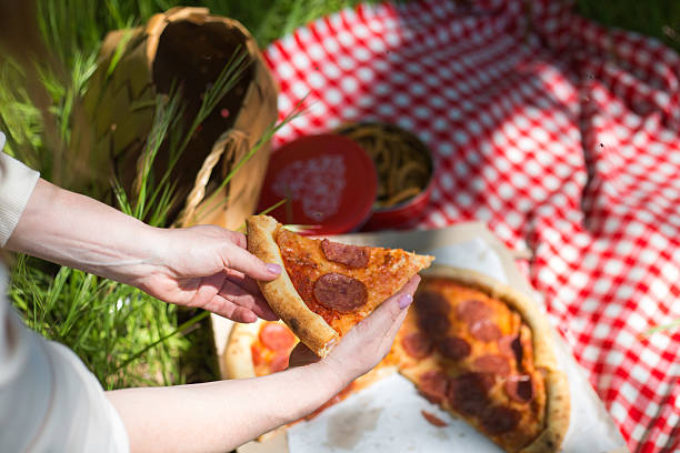 Woman eating pepperoni pizza during picnic on grass
