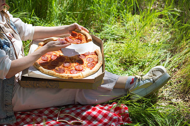 Woman eating pepperoni pizza during picnic on grass